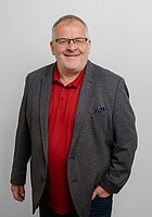 Ein Mann mit Brille lacht in die Kamera. Er trägt ein rotes Poloshirt und ein dunkelgraues Sakko.