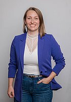 Eine Frau lacht in die Kamera. Sie trägt ein weißes Oberteil und einen violetten Blazer.