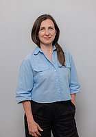 Eine Frau mit langen Haaren lächelt in die Kamera. Sie trägt eine hellblaue Bluse.