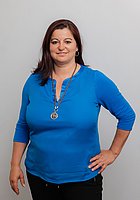 Eine Frau lacht in die Kamera. Sie trägt eine blaue Bluse und eine Halskette.