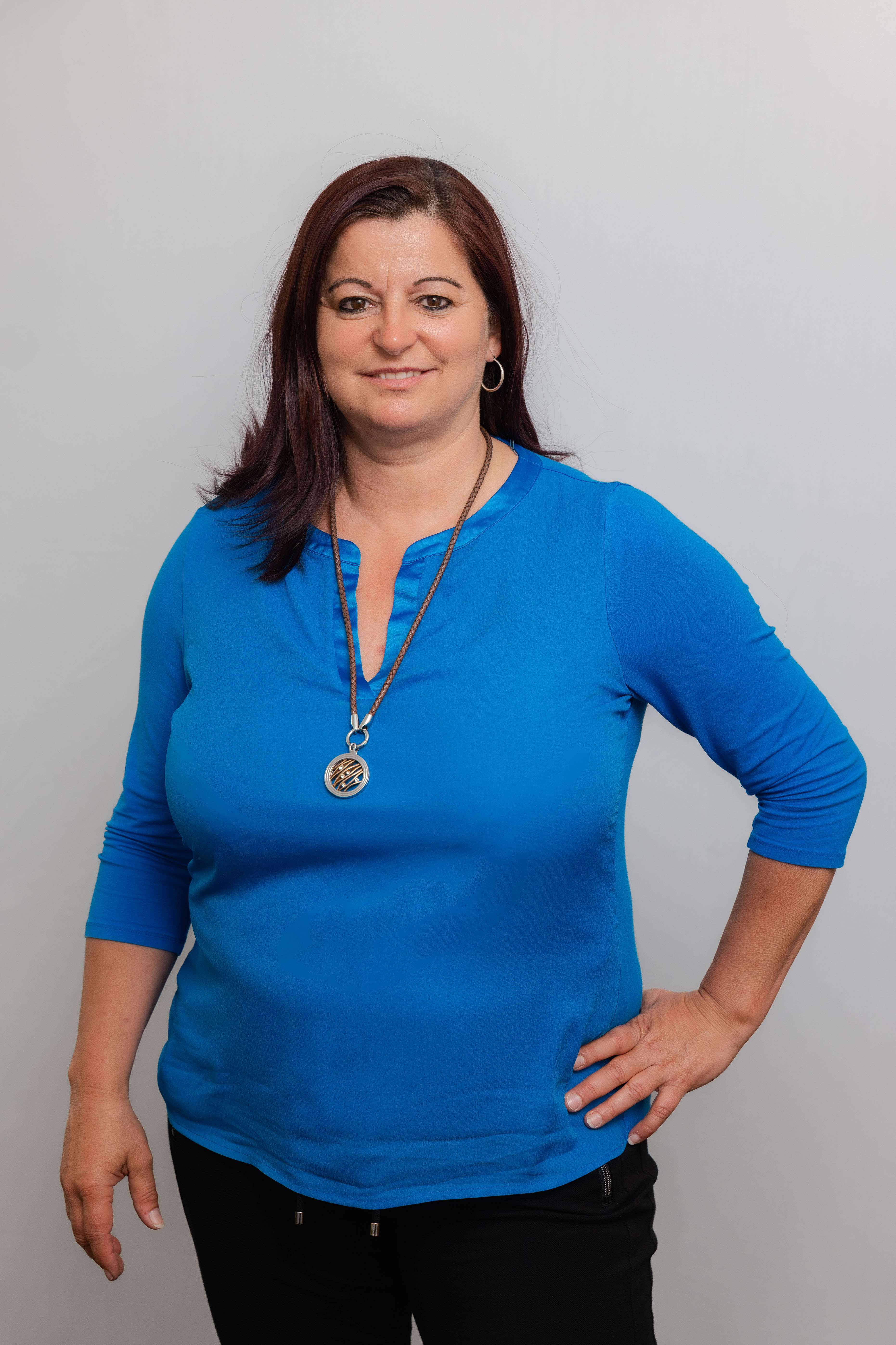 Eine Frau lacht in die Kamera. Sie trägt eine blaue Bluse und eine Halskette.