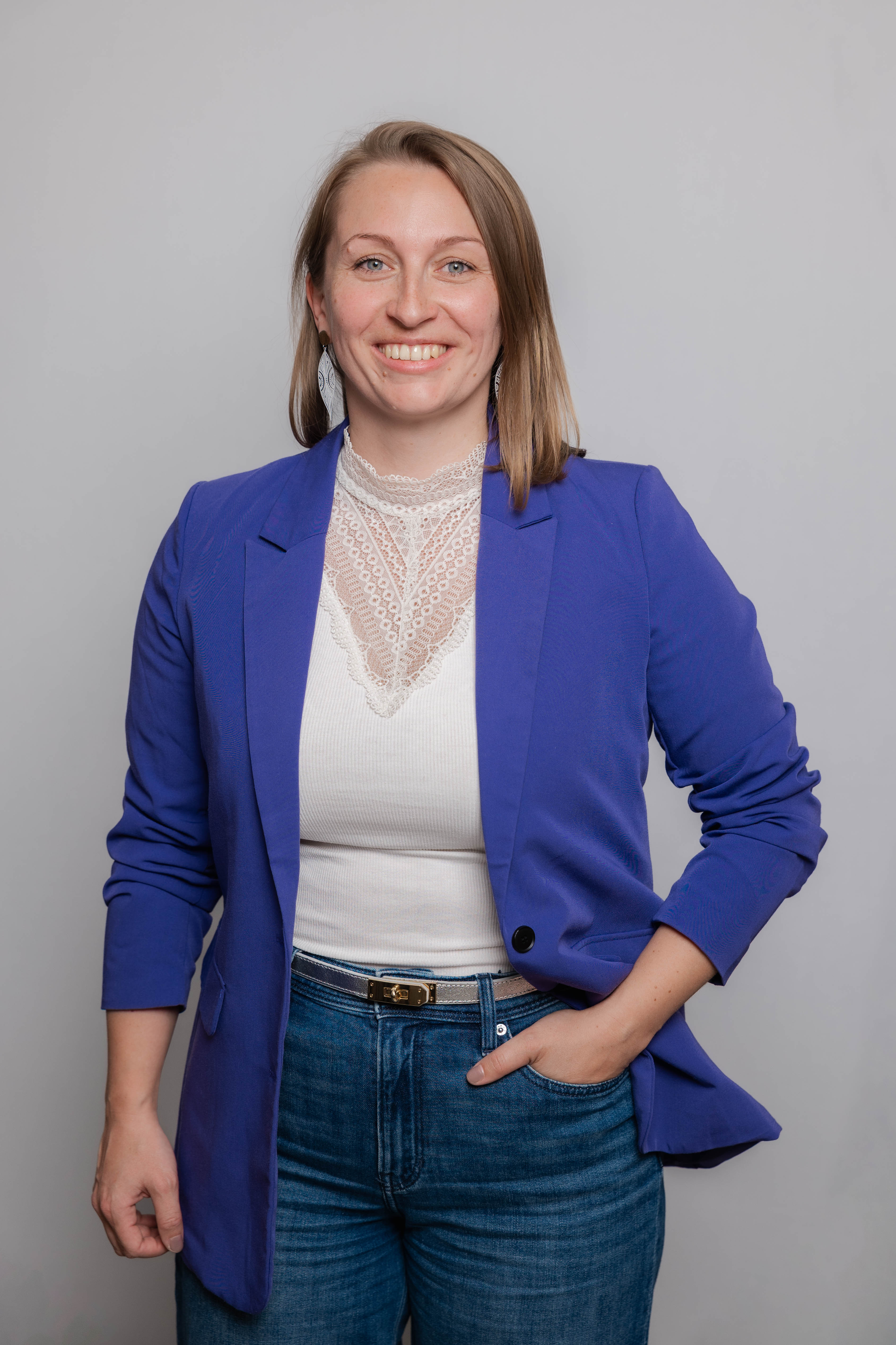 Eine Frau lacht in die Kamera. Sie trägt ein weißes Oberteil und einen violetten Blazer.