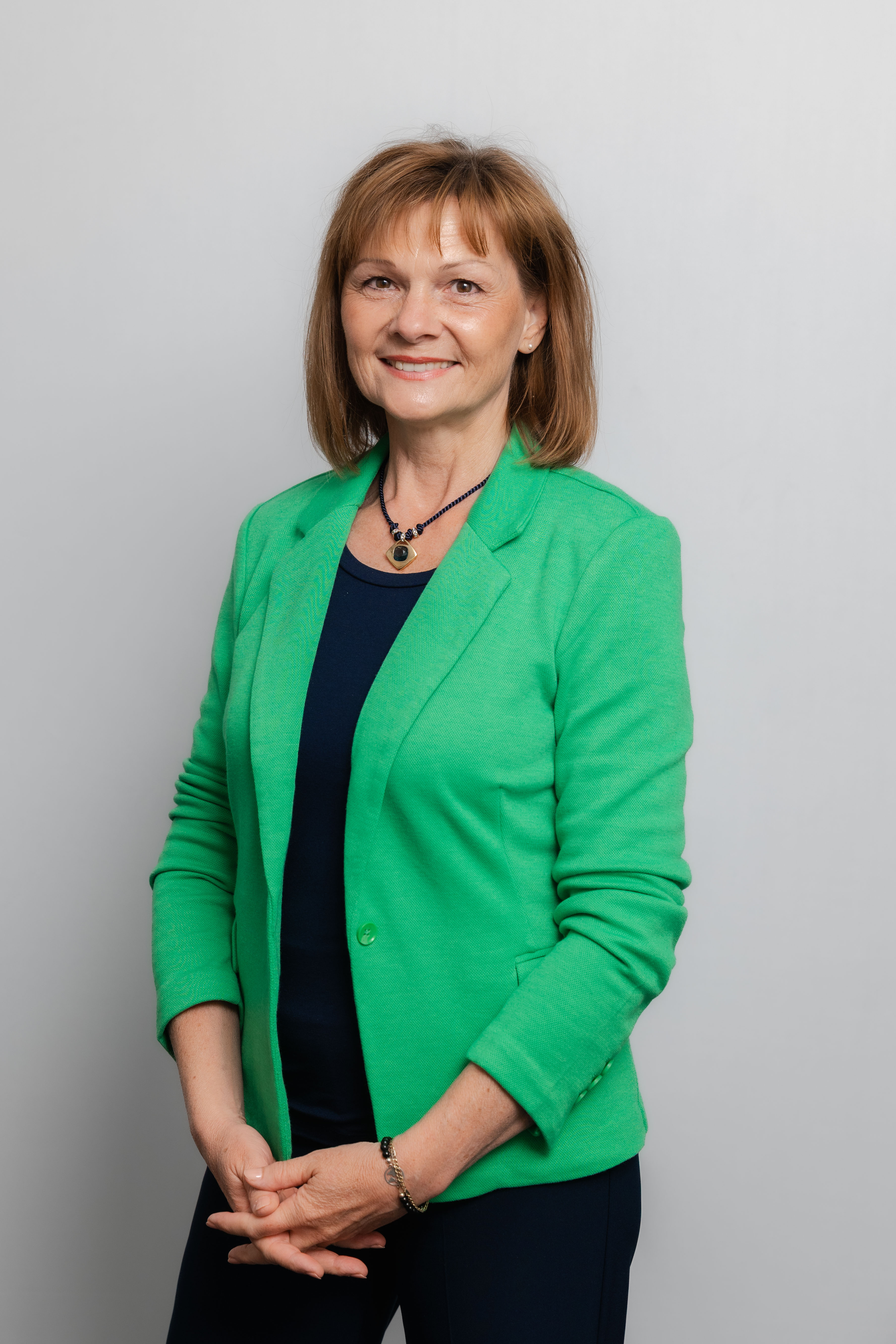 Eine Frau lacht in die Kamera. Sie trägt ein schwarzes Oberteil und einen grünen Blazer.