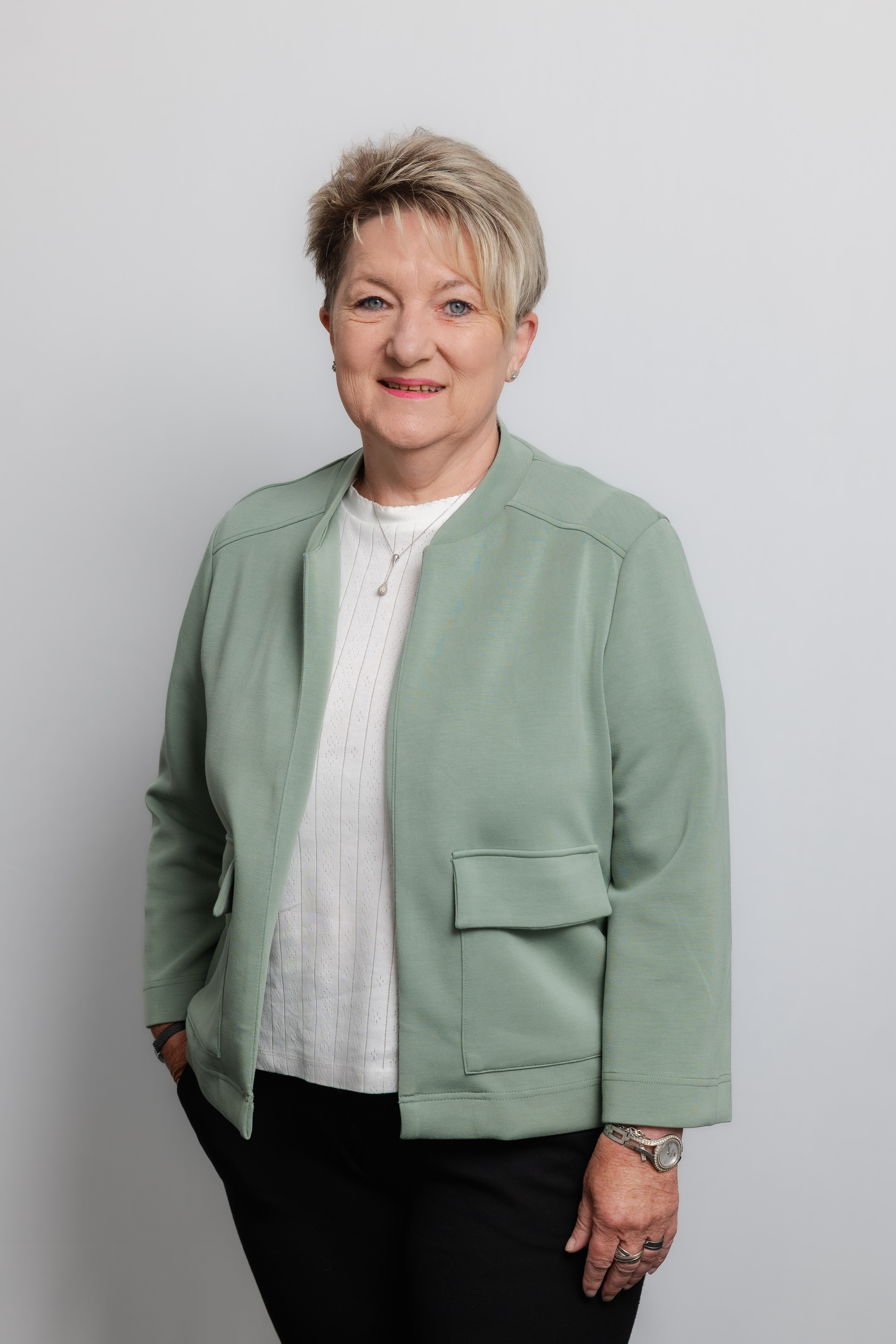 Eine Frau mit Kurzhaarschnitt lacht in die Kamera. Sie trägt ein weißes Oberteil und einen mintgrünen Blazer darüber.
