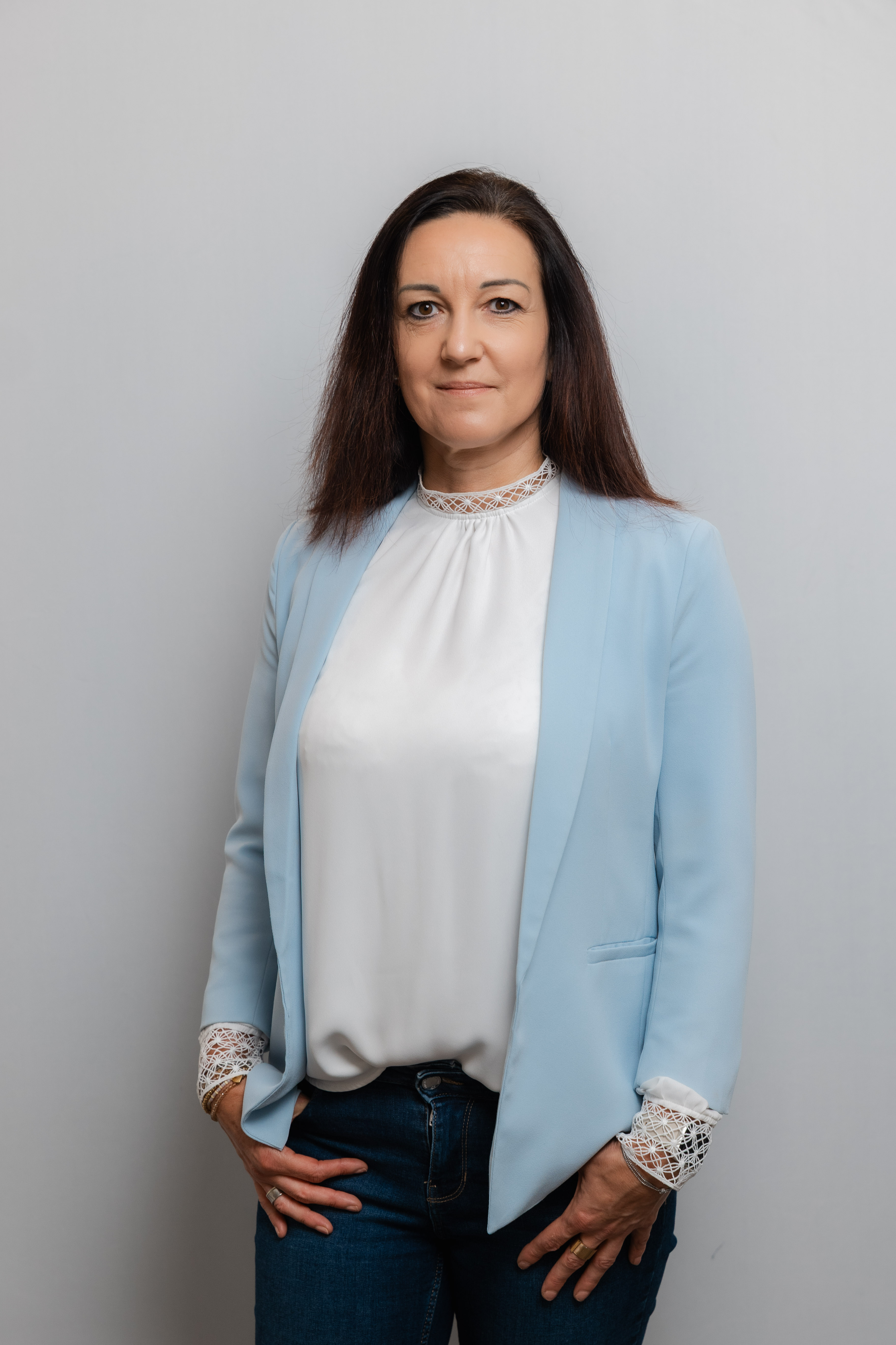Eine Frau mit langen dunklen Haaren lacht in die Kamera. Sie trägt eine weiße Bluse und einen hellblauen Blazer.