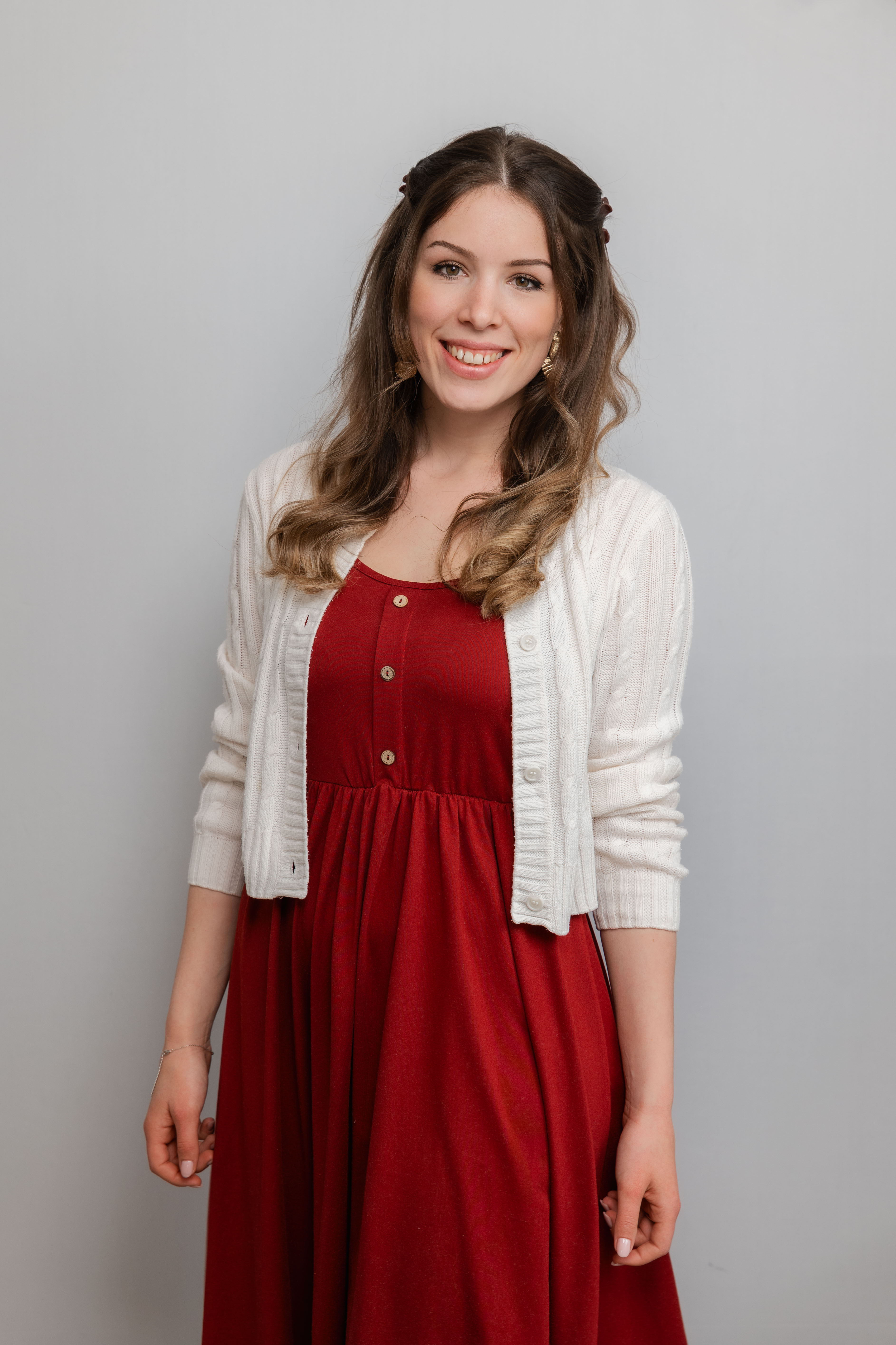 Eine Frau mit langen Locken lacht in die Kamera. Sie trägt ein rotes Kleid und eine weiße Weste darüber.